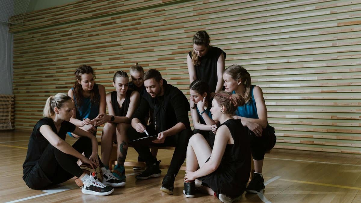 Female basketball team listening to coach's strategy session indoors.