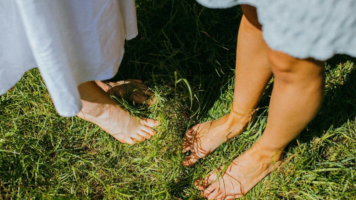 Two people enjoying the outdoor serenity while standing barefoot on lush green grass.