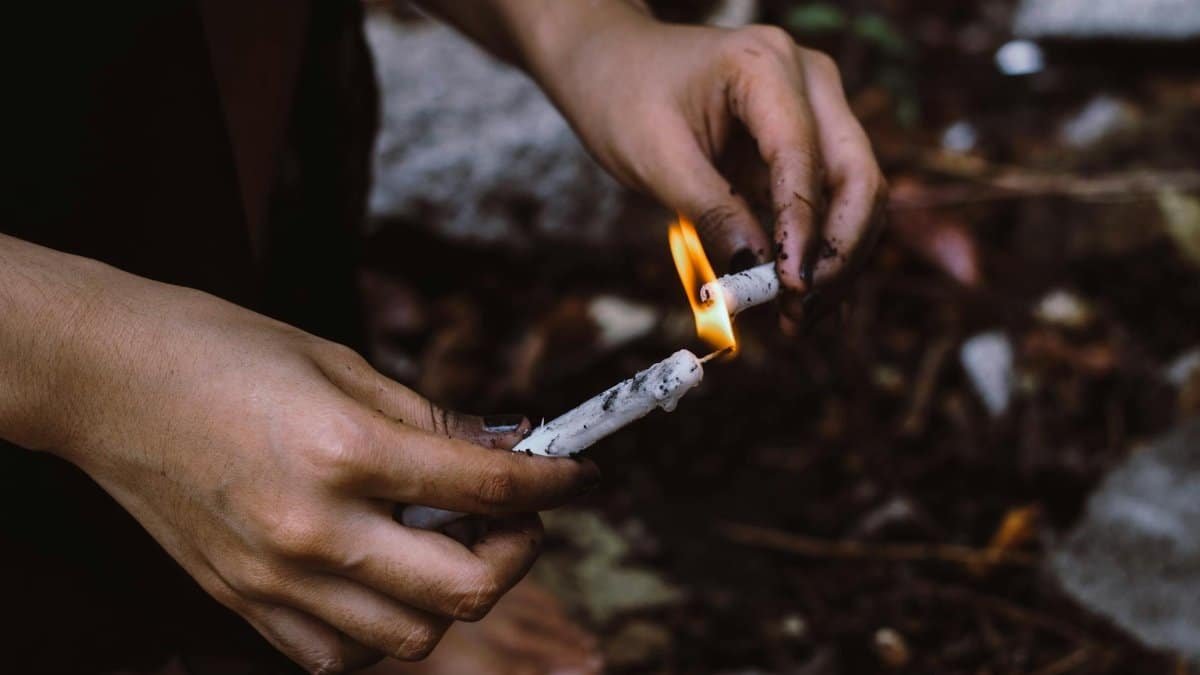A person lighting white candles outdoors, focusing on hands and flame against a natural background.