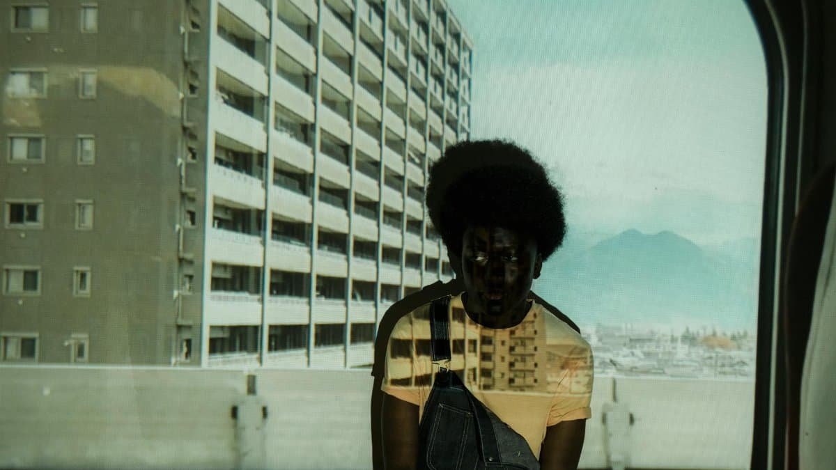 A man reflected in a train window with cityscape and mountains in the background.