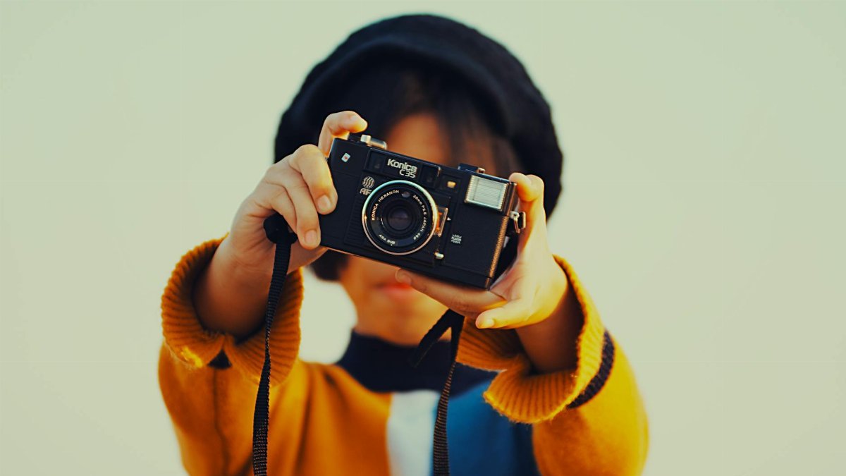 A young child holding a vintage Konica camera, showcasing retro technology.