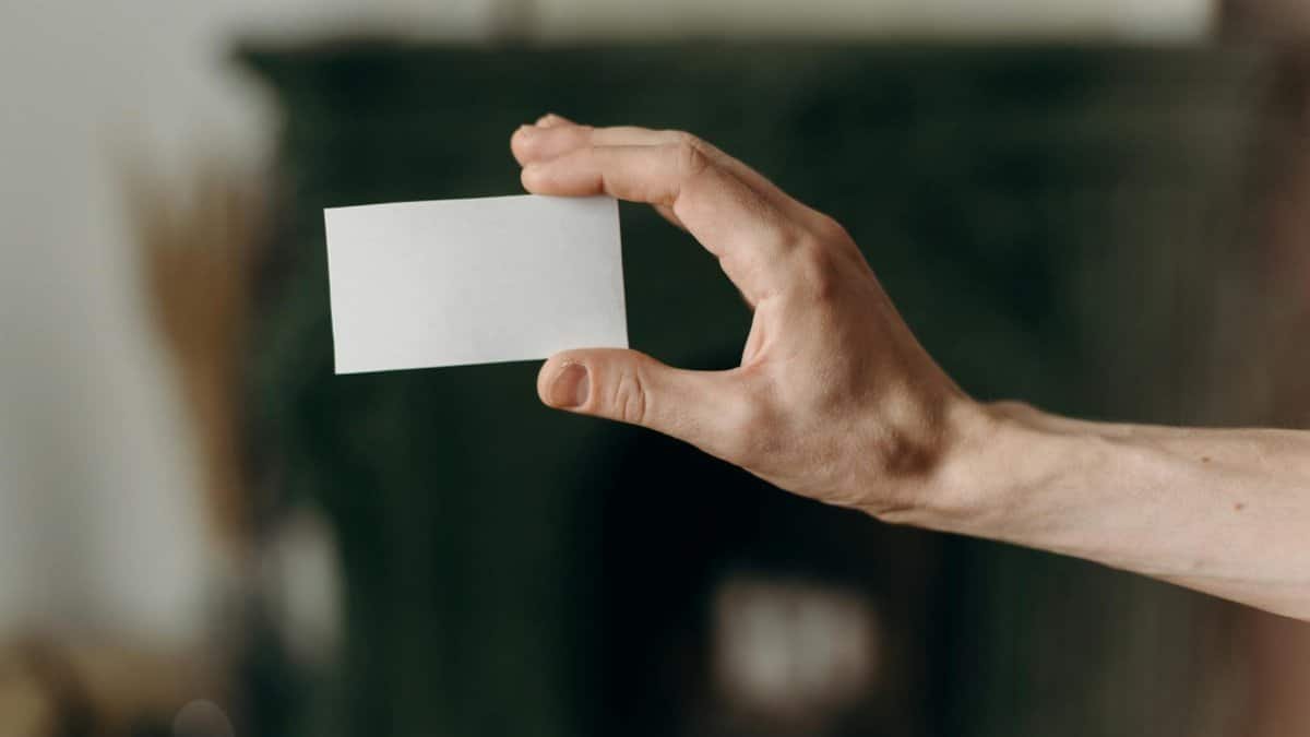 A hand holding a blank business card against a blurred indoor background, ideal for mockups.