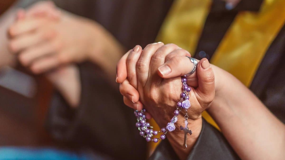A close-up of two people holding a rosary, symbolizing prayer and faith.