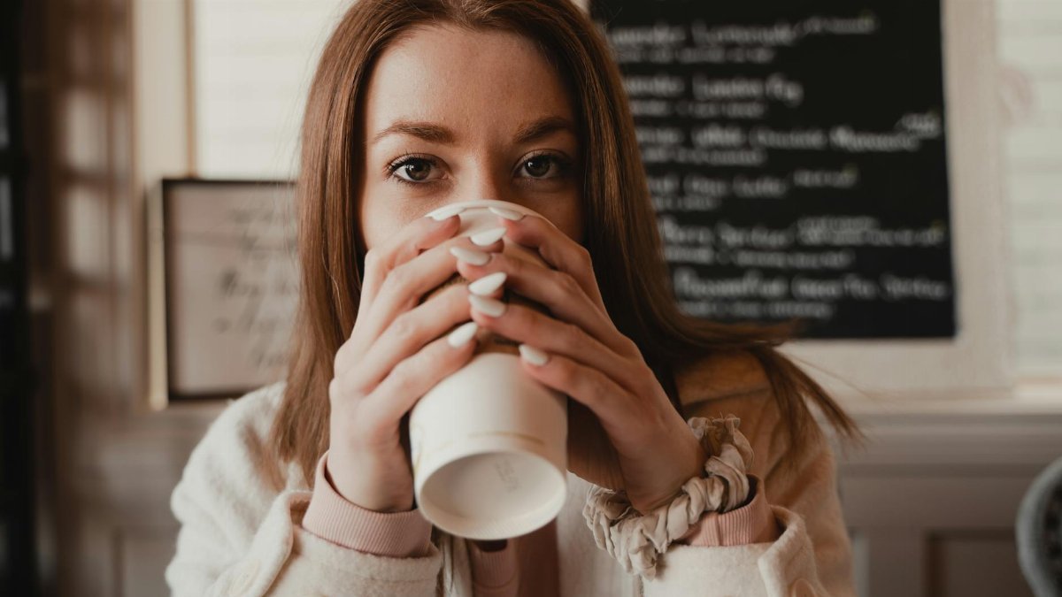 A young woman holding a cup, savoring her hot drink in a cozy indoor setting.
