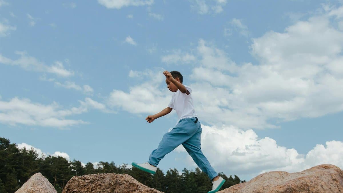 Young boy in motion, joyfully jumping on natural rocks under a bright blue sky.