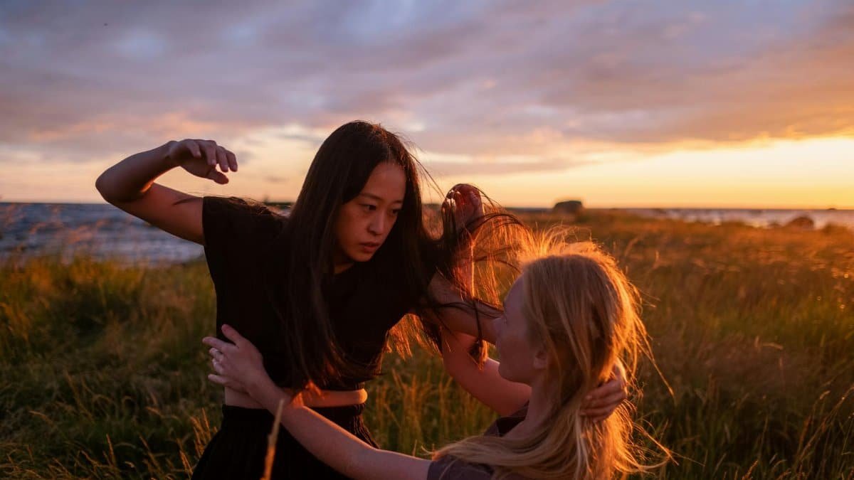 Two women engage in a dynamic moment at sunset, surrounded by a serene field.