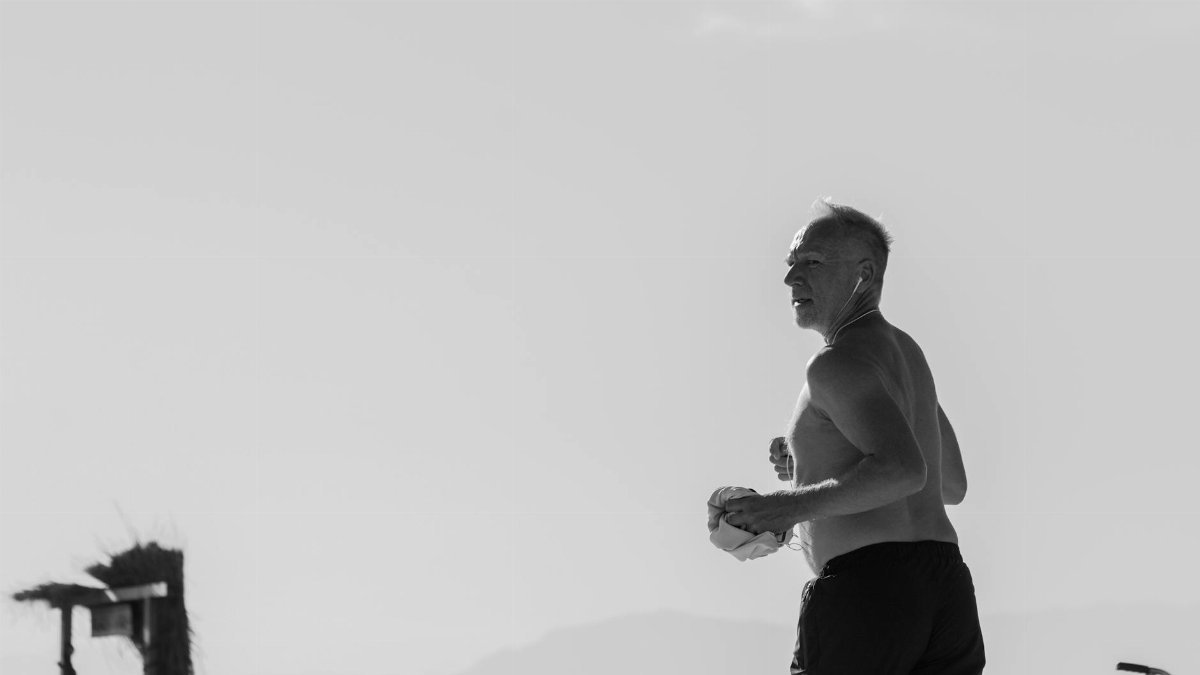 Dynamic monochrome image of an elderly man jogging along a beach, emphasizing fitness and lifestyle.