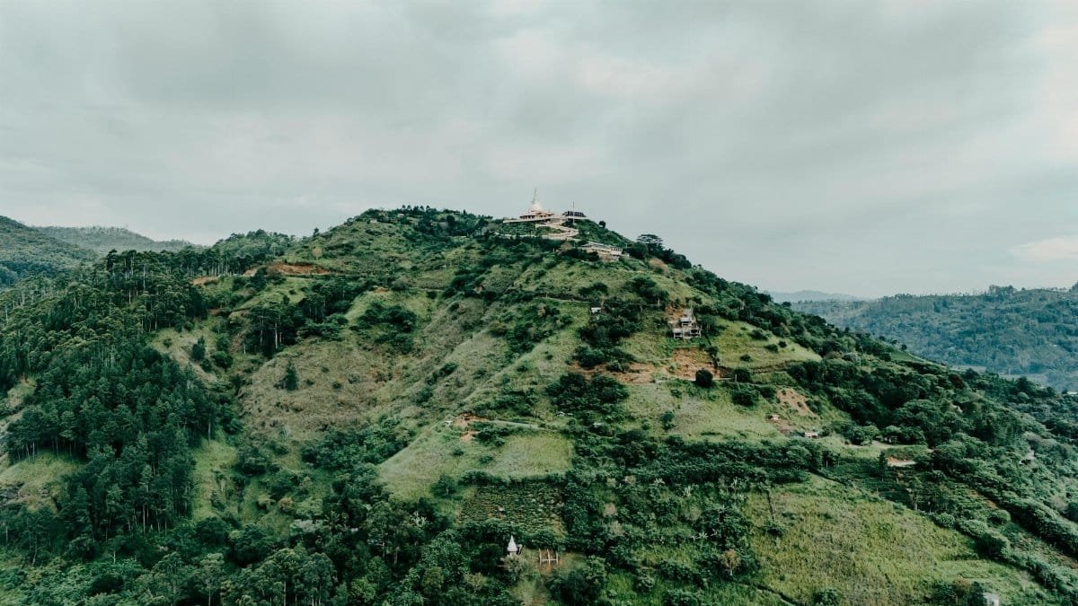Breathtaking aerial view of a lush, green mountain landscape in Sri Lanka, featuring a distant temple.