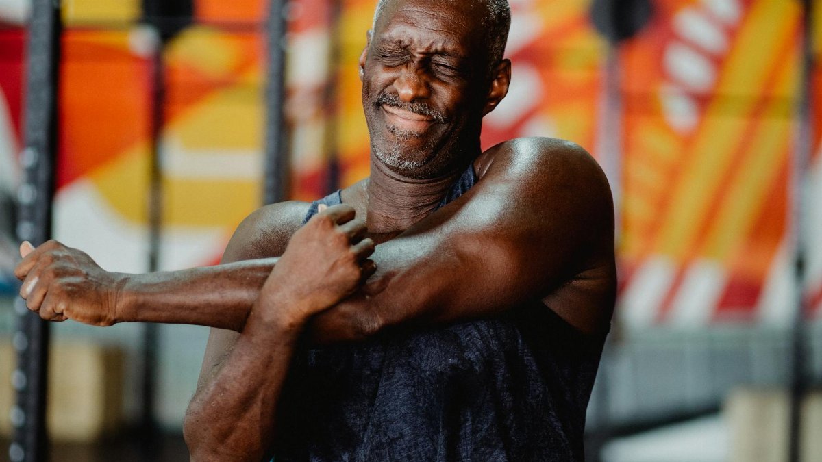 An elderly man stretches his arm indoors, embodying strength and wellness.