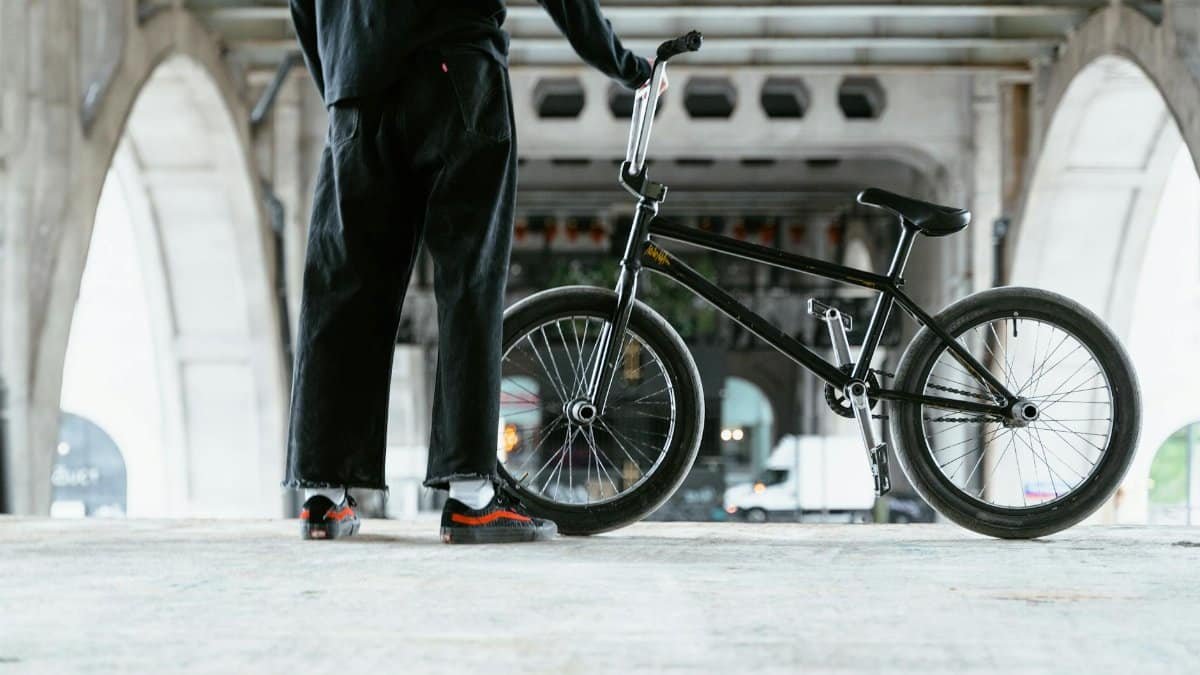 BMX biker standing with bicycle under urban bridge, ready for action and adventure.