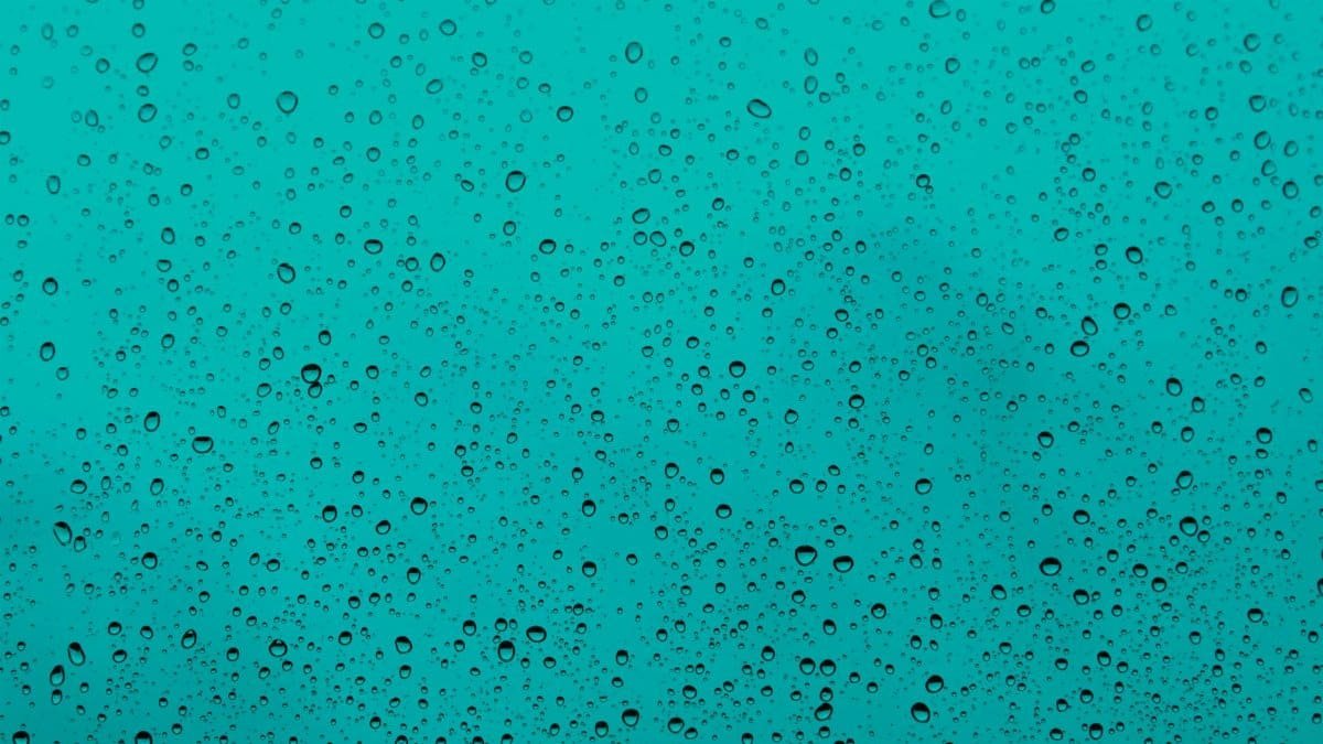 Close-up of water droplets on a teal glass window, capturing the beauty of rain.
