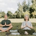 Senior couple meditating on yoga mats in a serene park setting, enjoying peaceful yoga practice.