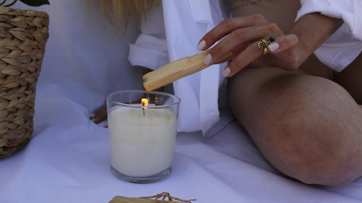 Woman using palo santo with a candle for relaxation. Cozy indoor setup.