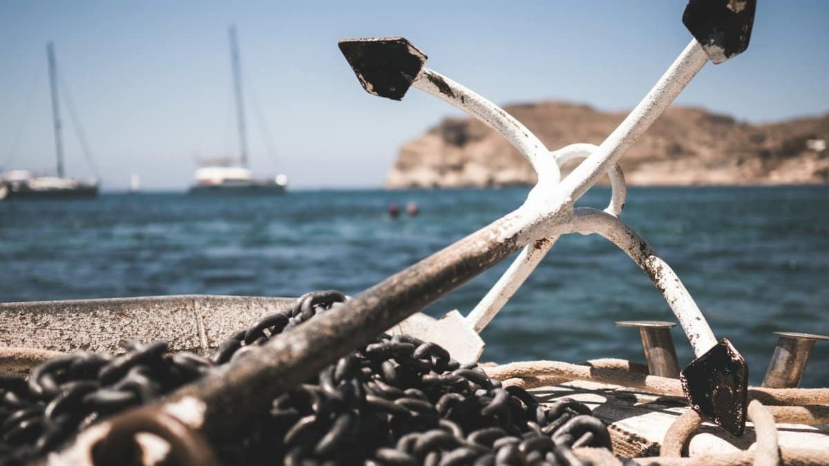 Close-up of boat anchor and chains with ocean and sailboats in the background.