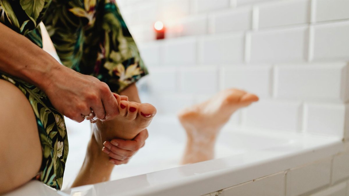 A soothing foot massage being given in a bath with white tiled walls and a relaxed atmosphere.
