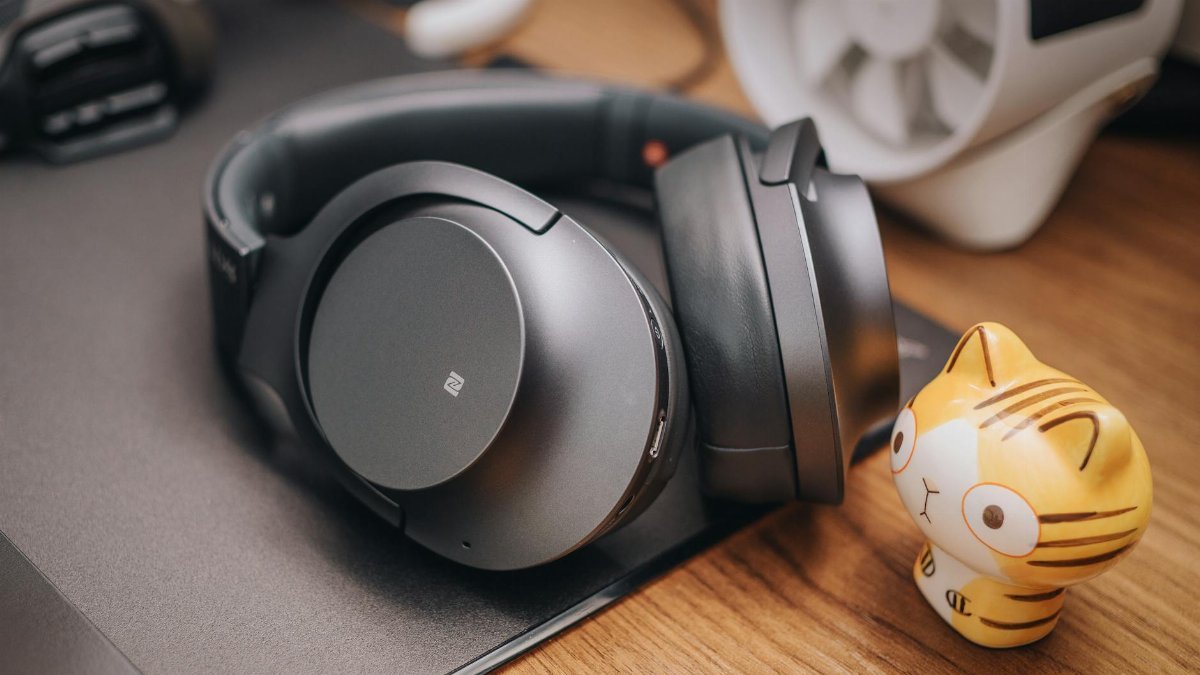 Stylish wireless headphones on a wooden desk with a cute cat figurine. Perfect for tech enthusiasts.