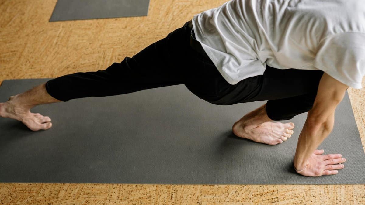 A man performing a crescent lunge pose on a yoga mat indoors, emphasizing balance and fitness.