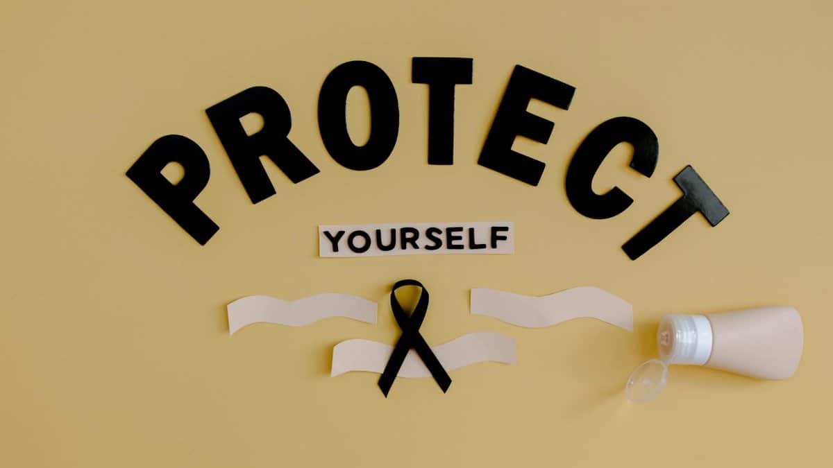 Black ribbon and lotion with 'Protect Yourself' on a yellow background representing health awareness.