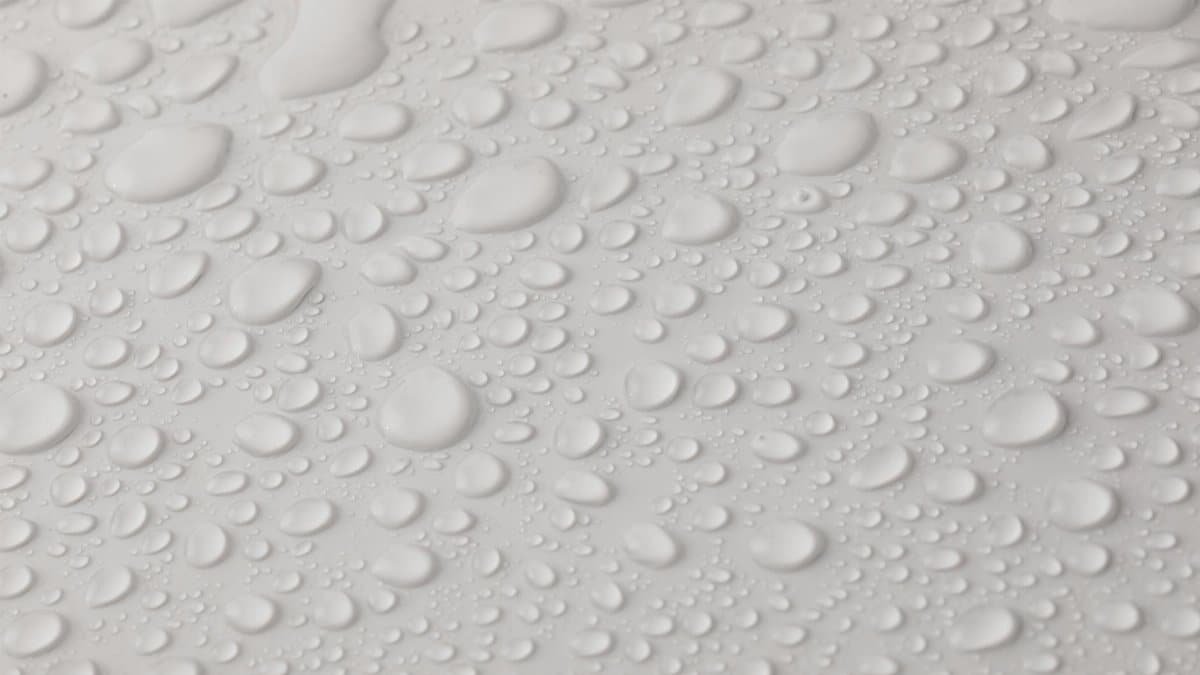 Closeup top view of plain wet abstract surface with small dripped water drops of different shapes placed on white background
