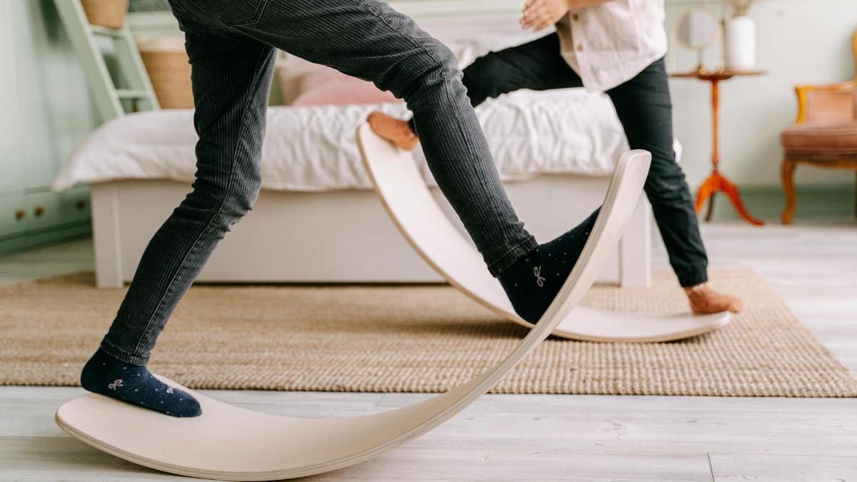 Two kids balancing on wooden balance boards in a cozy indoor setting for playful learning.