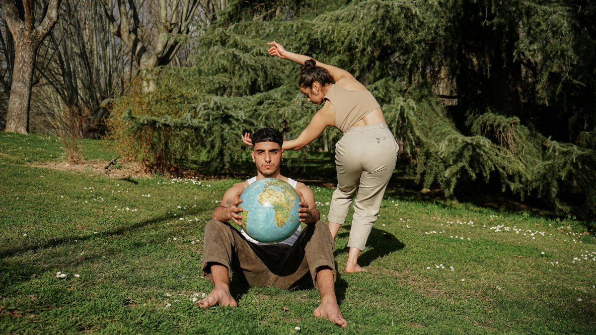 Two adults engaging in interpretive dance outdoors with a globe symbolizing unity and nature.