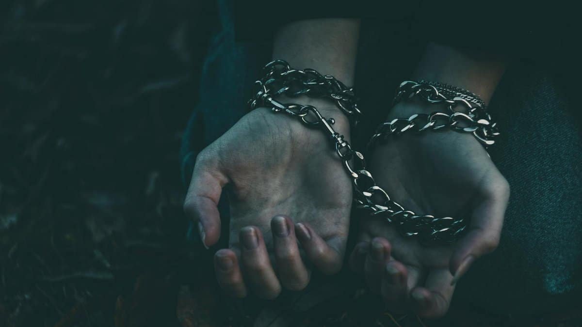 A dramatic close-up image of hands bound by silver chains, symbolizing captivity or struggle.