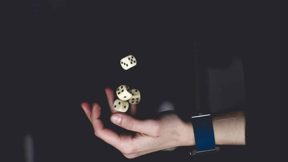 A close-up of a hand tossing several dice against a dark background, symbolizing chance and luck.