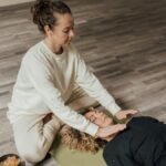 Woman practicing Reiki healing therapy on another woman lying indoors on a yoga mat.