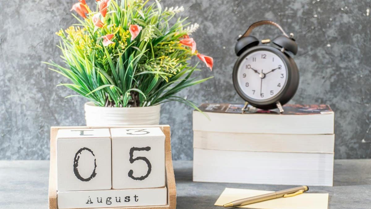 Stylish decorative arrangement featuring a calendar, clock, books, and a flower vase on a wooden surface.