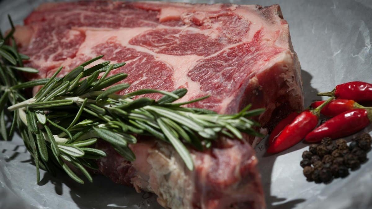 Close-up of a raw steak garnished with rosemary and chilies, ideal for cooking concepts.