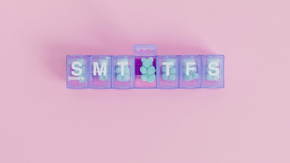 Top view of a weekly pill organizer filled with pills on a pink background.