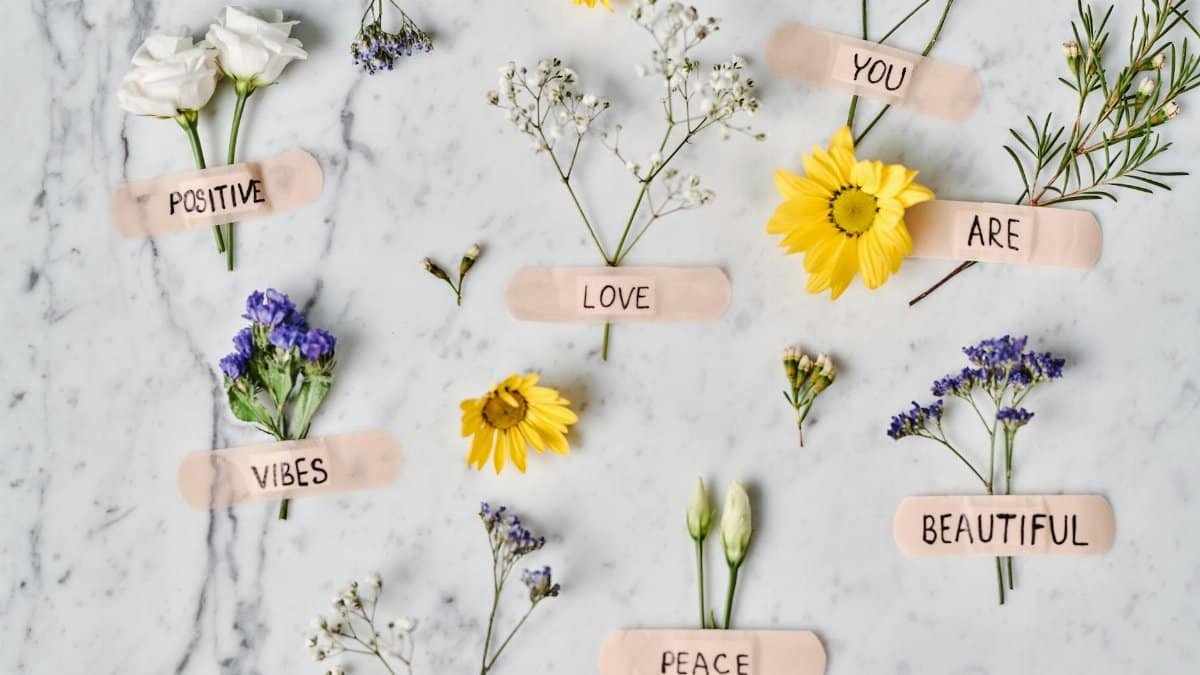 Floral flat lay with positive words on band-aids over a marble surface, promoting peace and love.