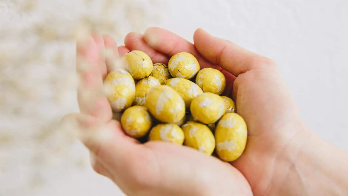 Close-up of hands holding yellow foil-wrapped chocolate eggs, perfect for Easter celebrations.