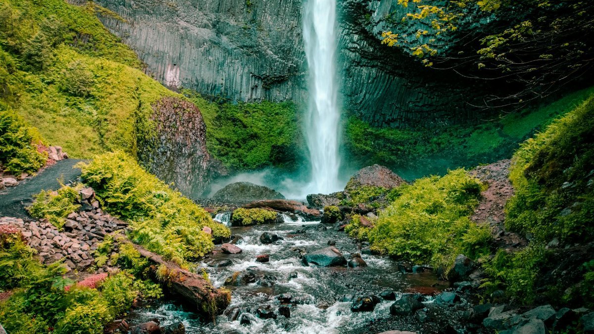 Majestic waterfall cascading down rocky cliff surrounded by vibrant greenery in a serene outdoor location.