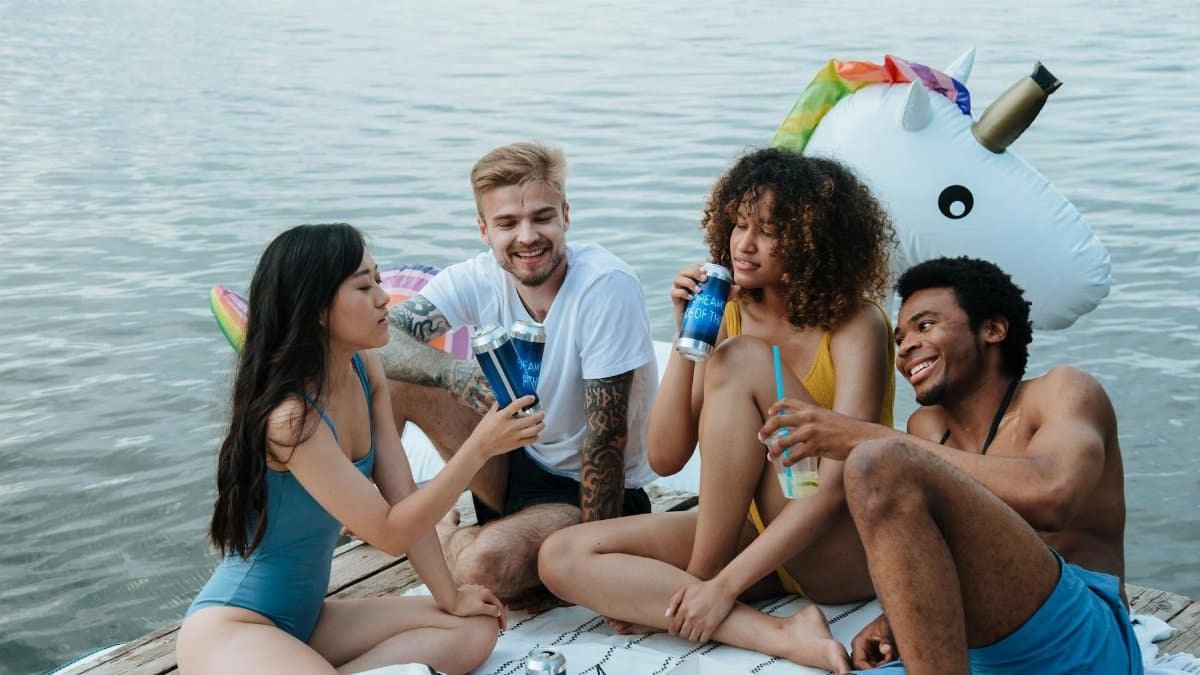 Group of friends relaxing on a dock with drinks during summer near a lake.