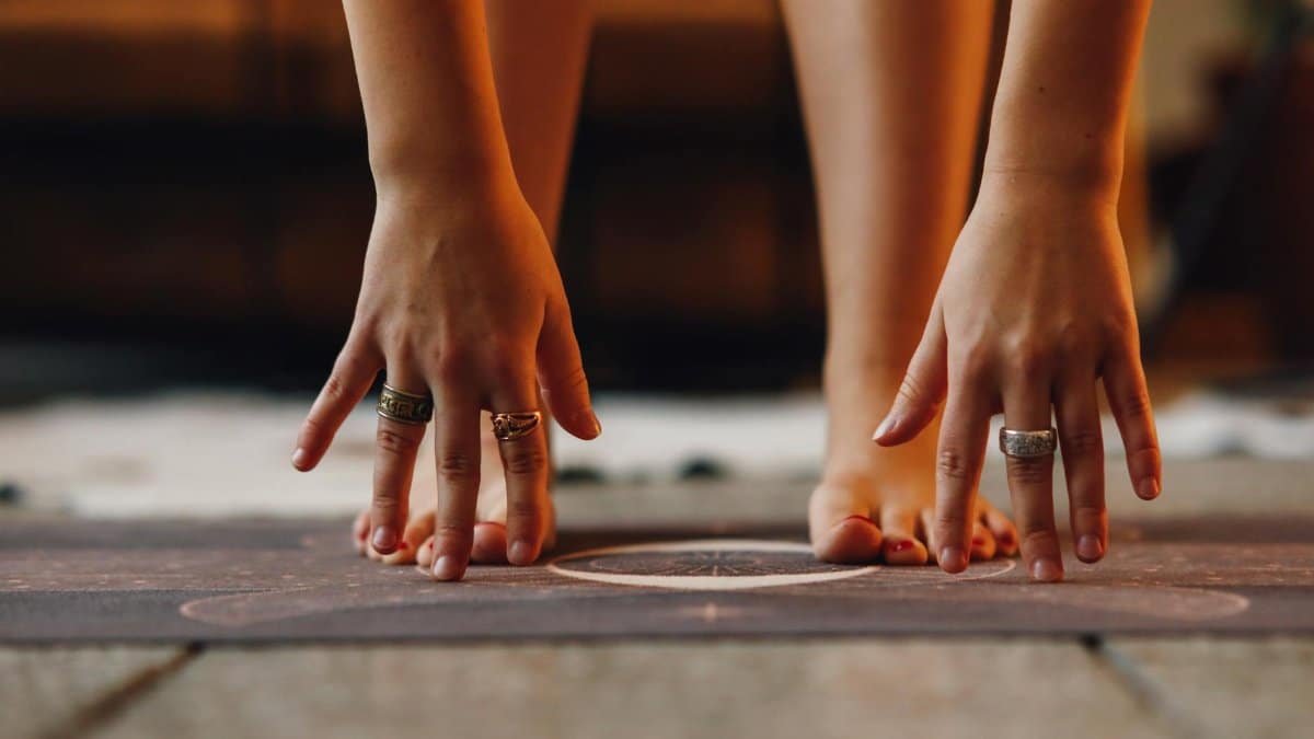 Close-up view of a person stretching hands and feet on a yoga mat indoors.
