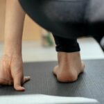 Back view of crop unrecognizable flexible female stretching legs and practicing yoga in Crescent Lunge on the Knee pose at home
