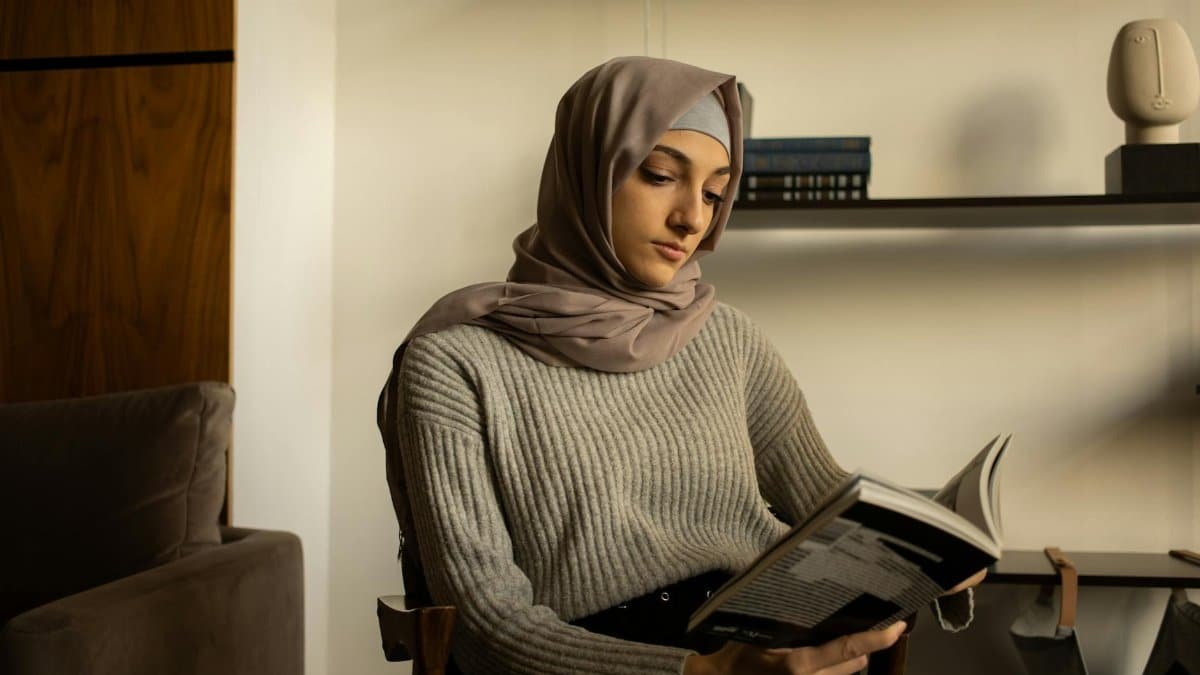 A woman wearing a hijab studies while sitting in a cozy interior