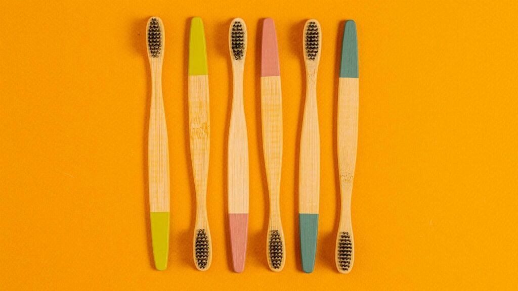 Six bamboo toothbrushes with colorful tips on a vibrant orange surface.