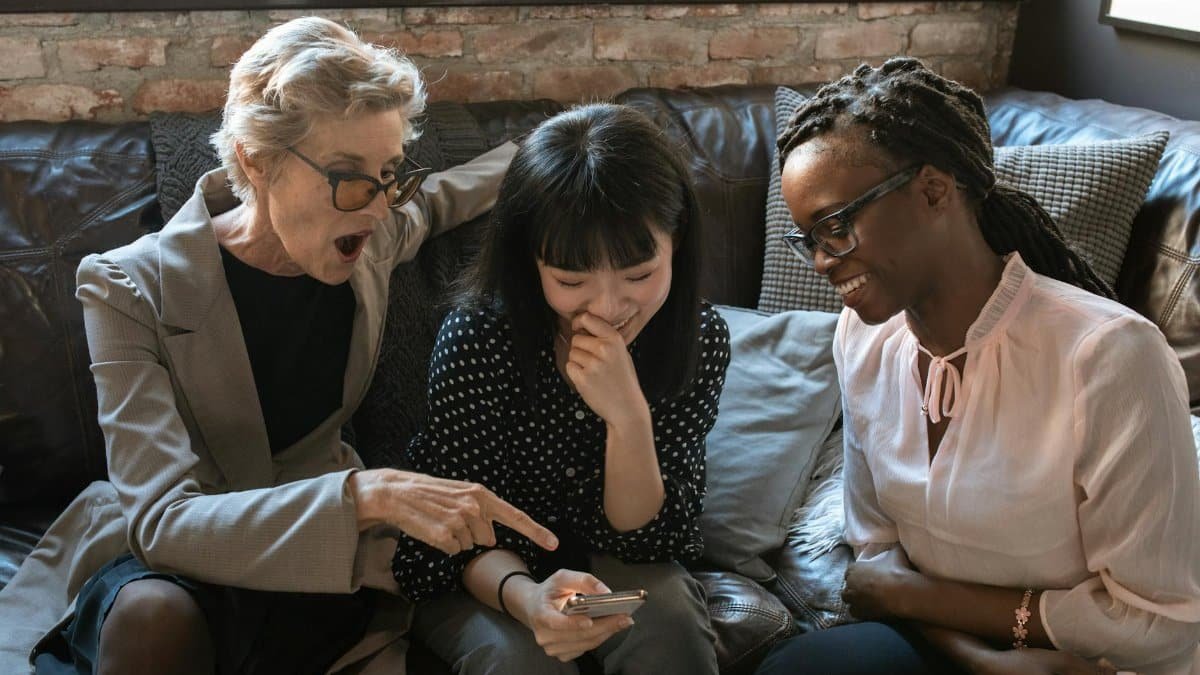 Three women of different ethnicities sharing a light-hearted moment indoors.