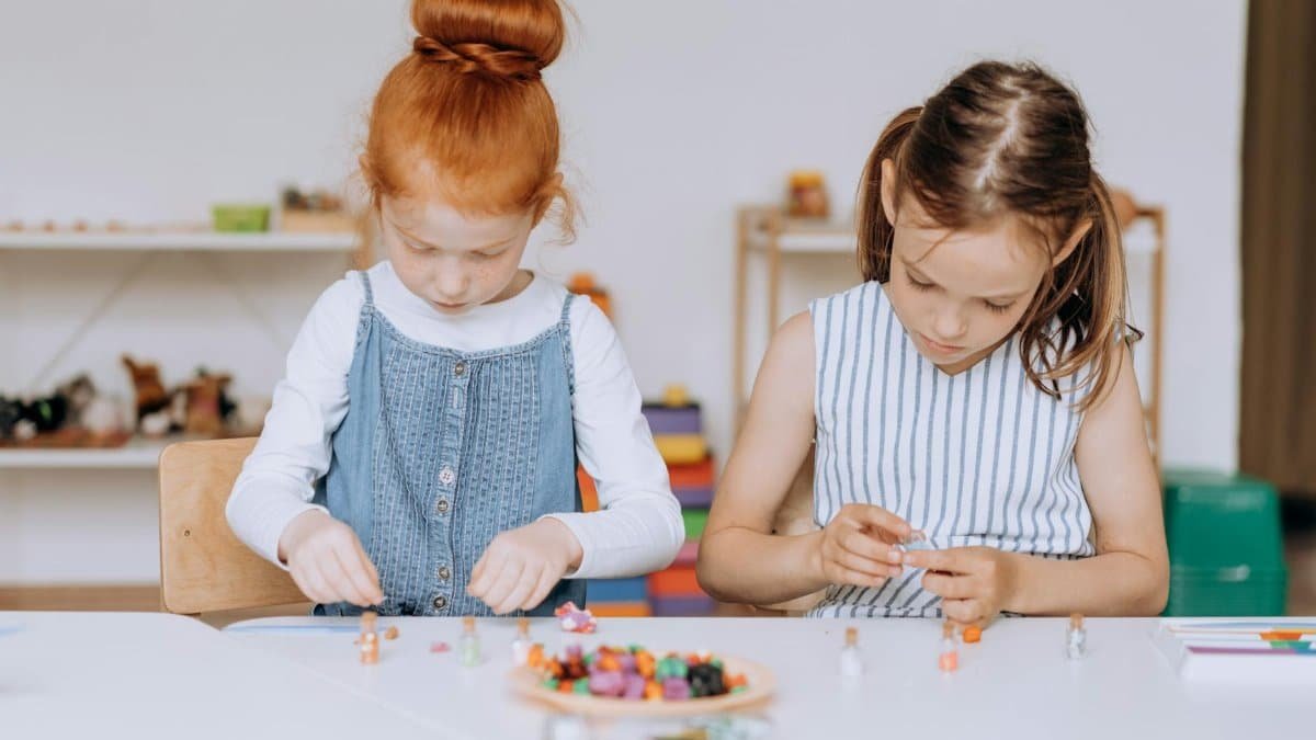 Two young girls actively engaged in a creative project at a classroom table, fostering education and creativity.
