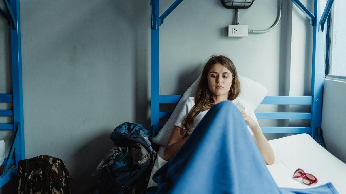 A young woman lies resting in a hospital bed, wrapped in a blue blanket, creating a calm and serene atmosphere.