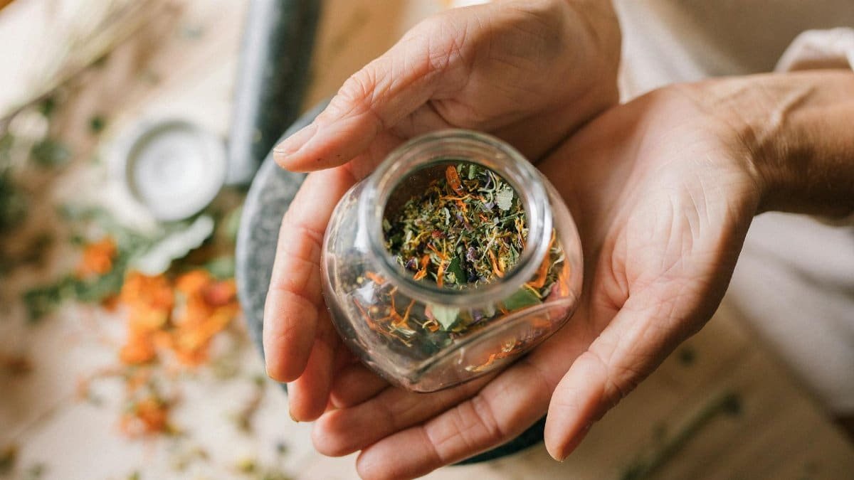 Close-up of hands holding a glass jar filled with colorful dried herbs.