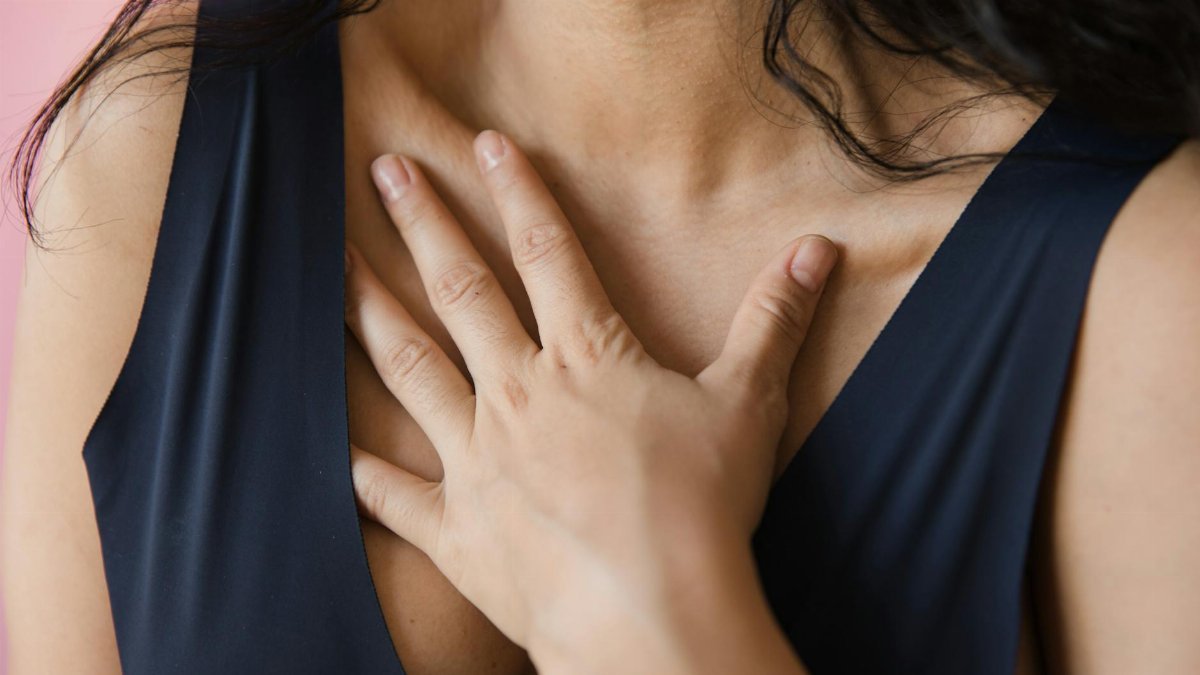Intimate close-up of a woman in a sleeveless blue top with a hand on her chest, conveying emotion.