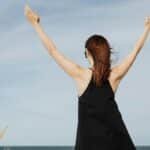 Woman raising hands in joy by the seaside in a black dress