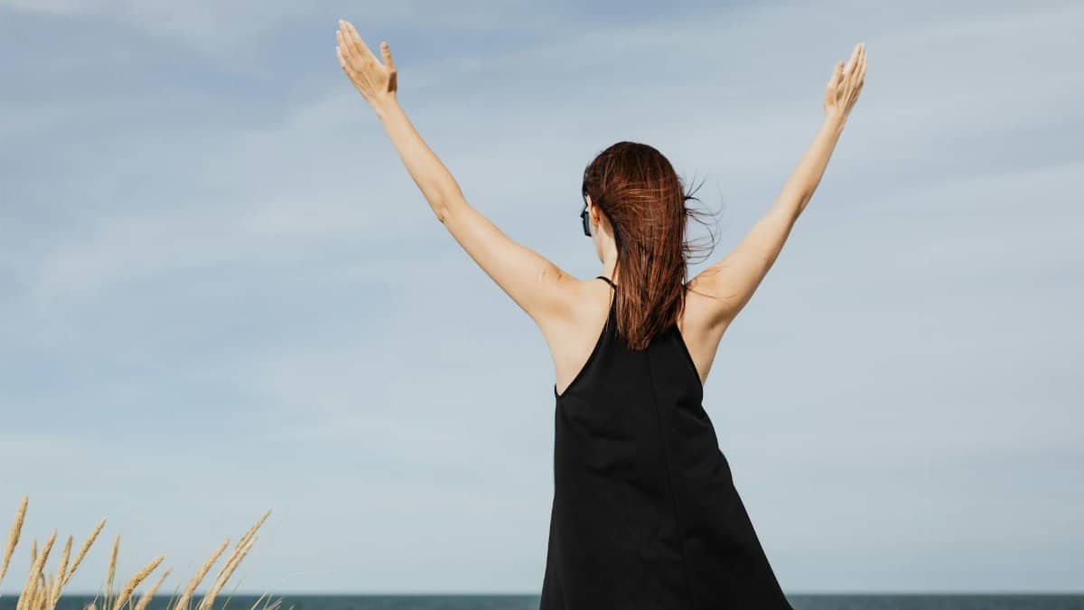 Woman raising hands in joy by the seaside in a black dress