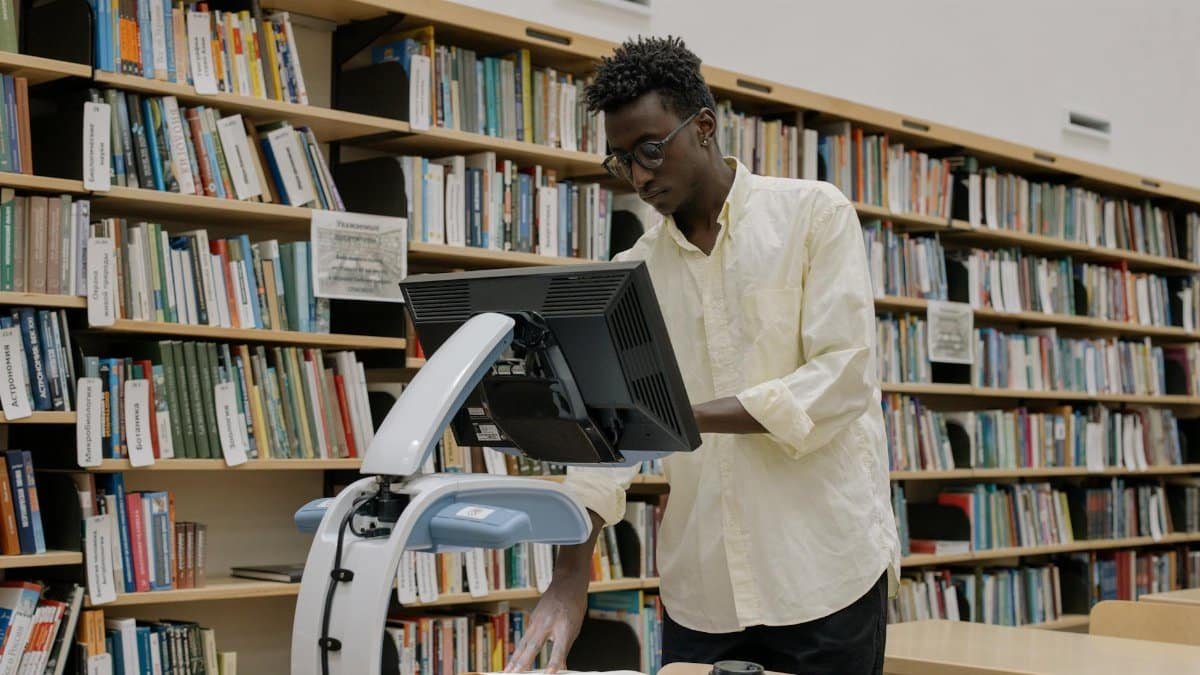 An African American man scanning books in a modern public library surrounded by bookshelves.