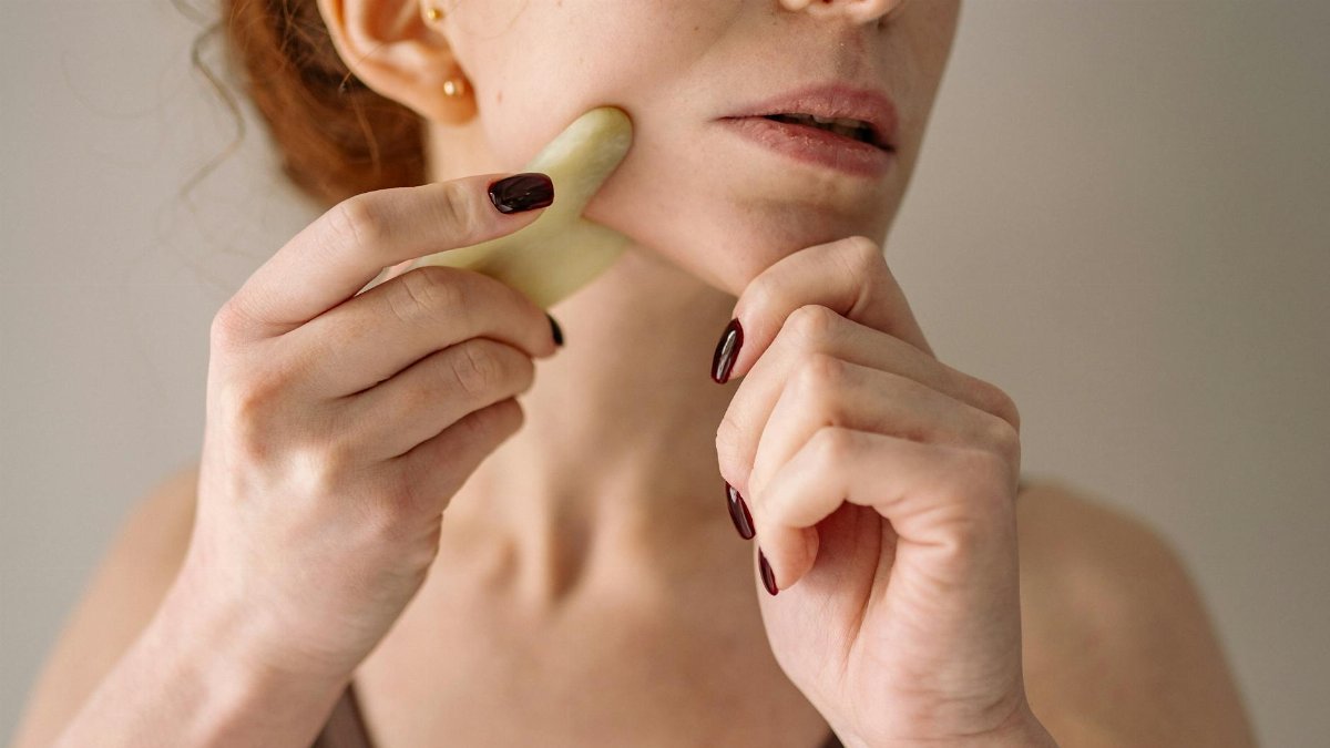 Close-up of a woman using a gua sha stone on her face, emphasizing self-care and beauty routine.