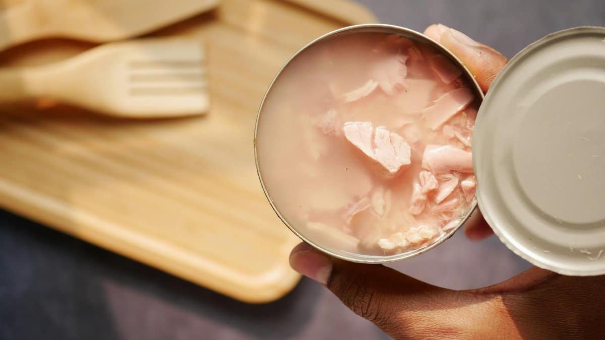 A close-up of an opened canned tuna held over a wooden cutting board and utensils.