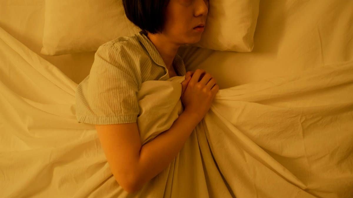 Side view of an Asian woman lying in bed, reflecting anxiety and insomnia in dim light.